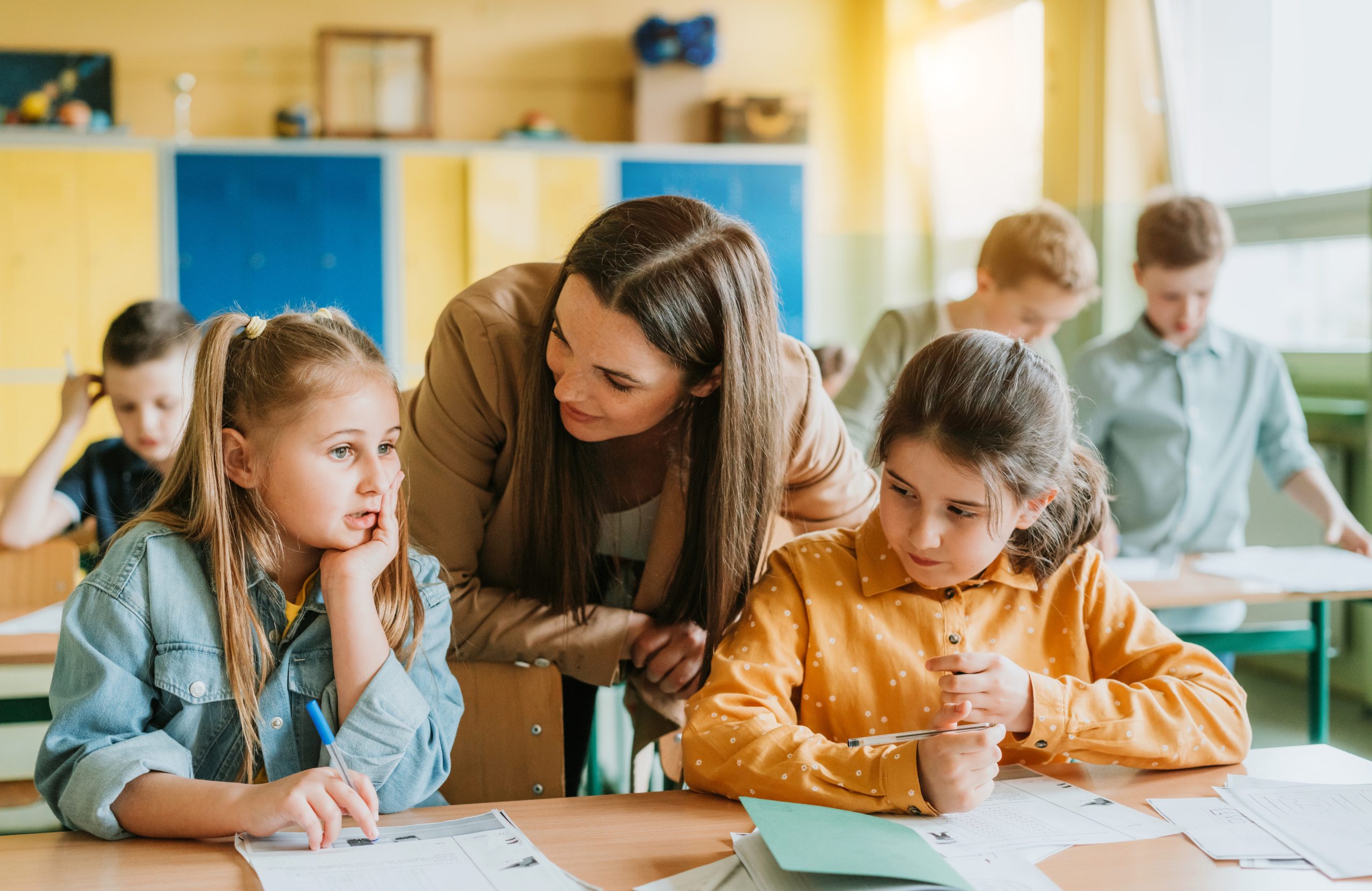 Female teacher assisting two young students in a classroom